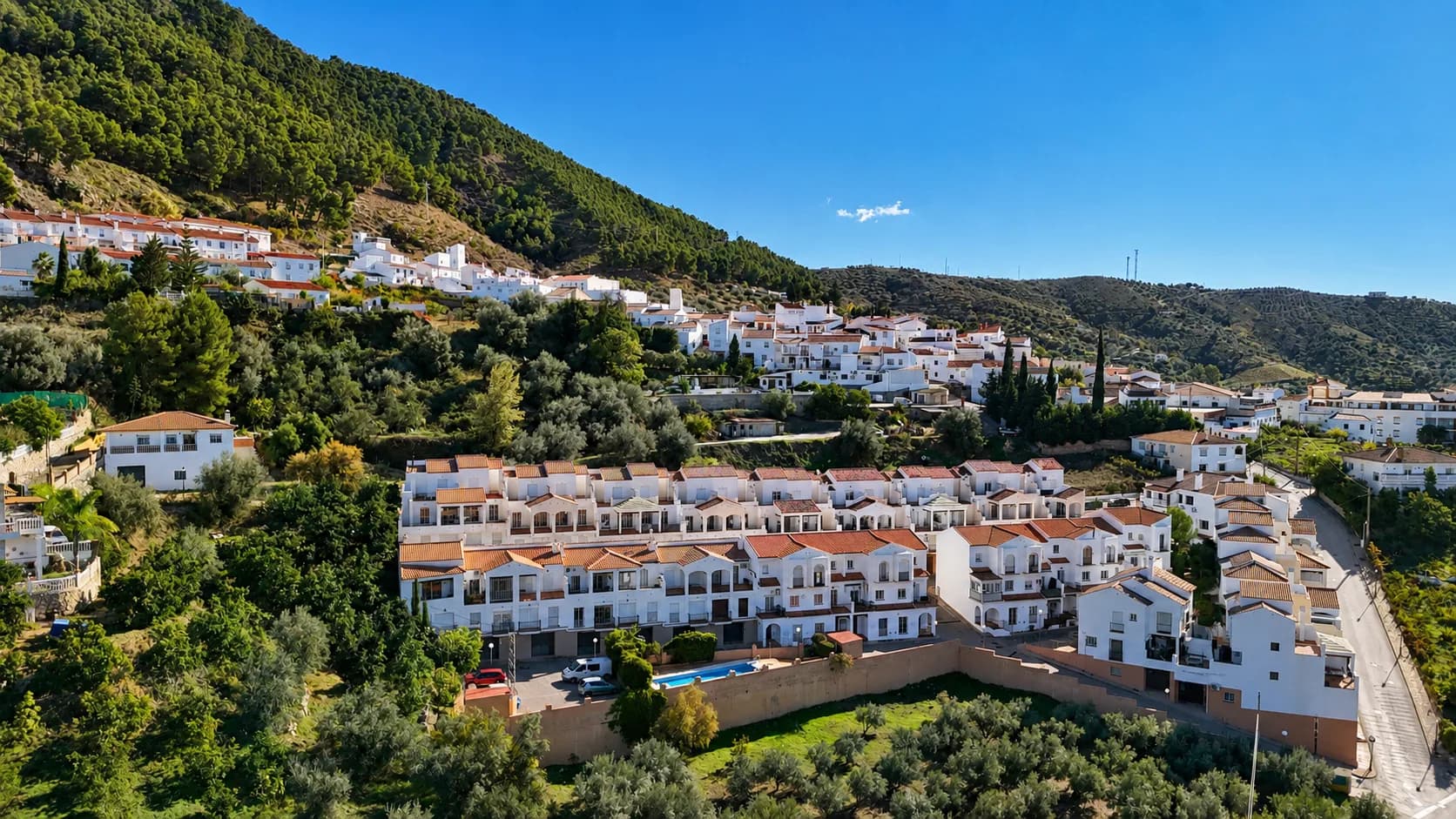Casas de vacaciones modernas con fachadas blancas, situadas entre colinas verdes en un soleado paisaje español.