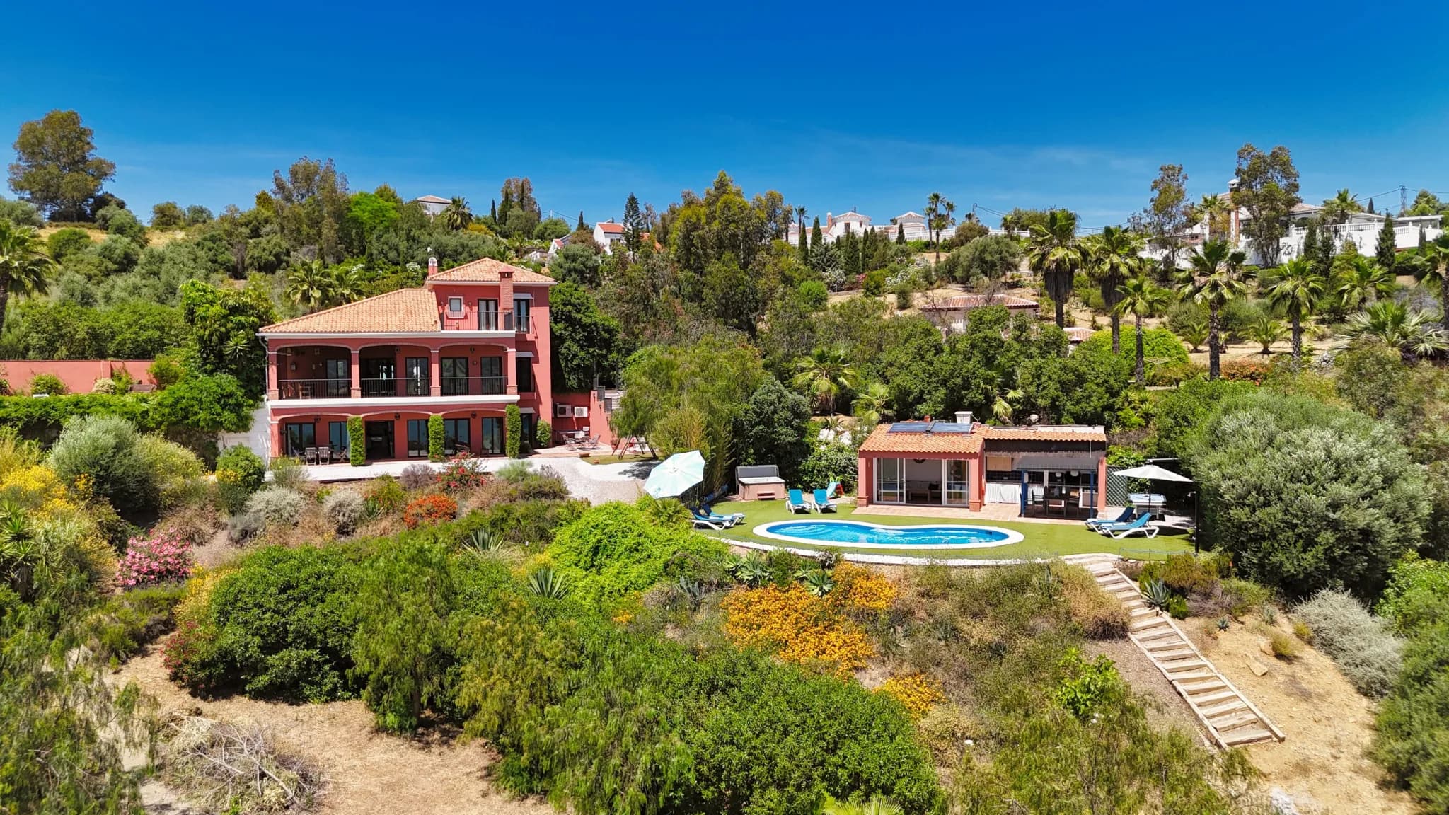 Amplia casa de vacaciones en España con piscina y exuberante jardín, rodeada de un hermoso entorno verde.