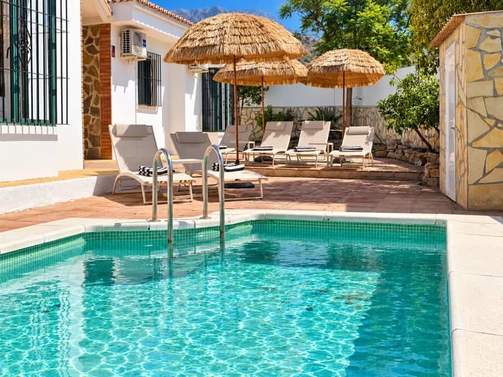 Sonniges Ferienhaus in Spanien mit einem Privatpool, Liegestühlen und Sonnenschirmen in grüner Umgebung.
