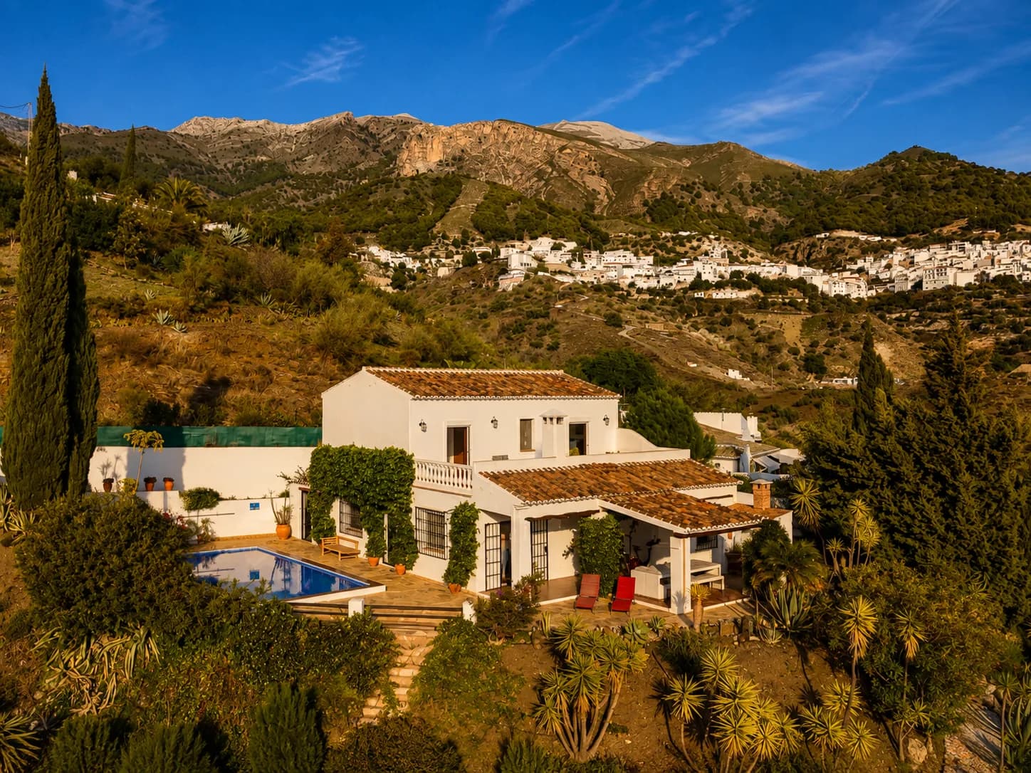 Preciosa casa de vacaciones con piscina, rodeada de naturaleza y con pueblos blancos de fondo en un entorno montañoso en España.